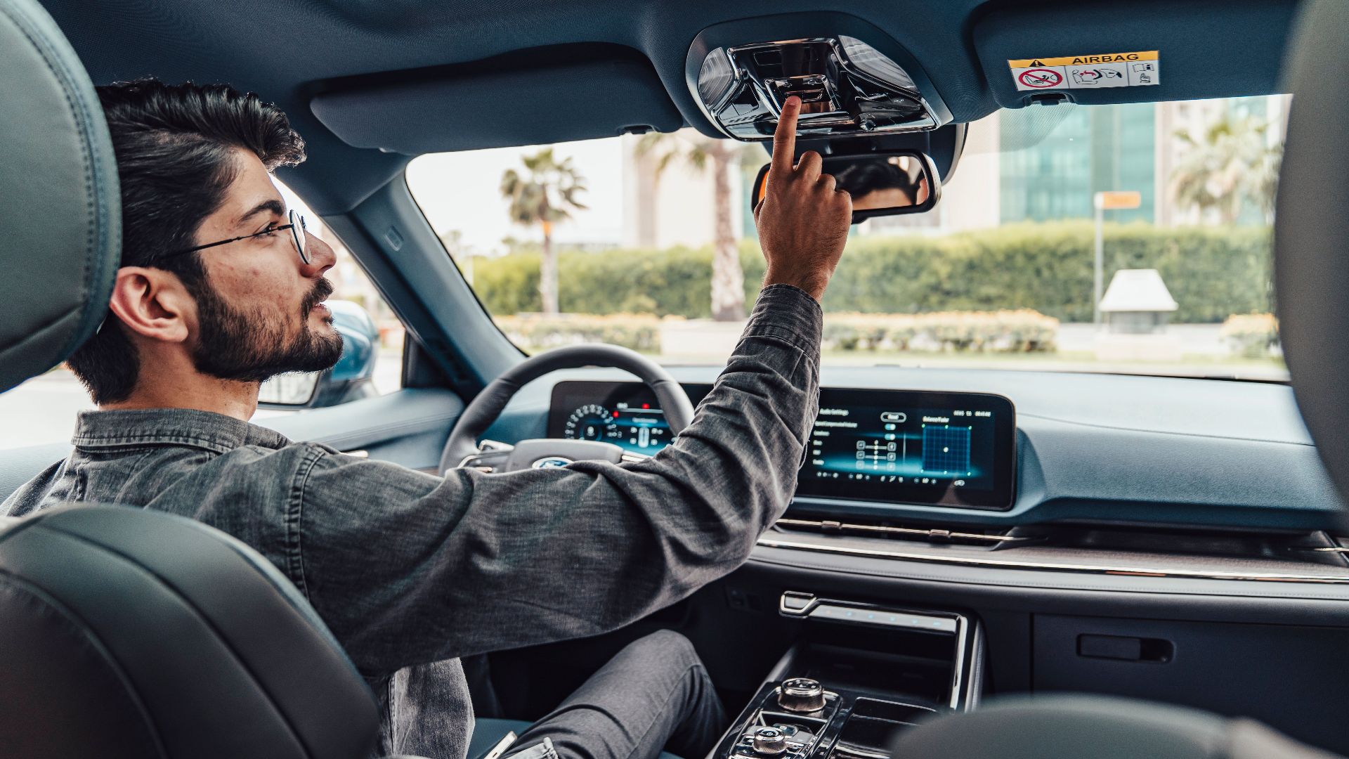 A man adjusts the interior features of a modern car while driving in Erbil, Iraq.