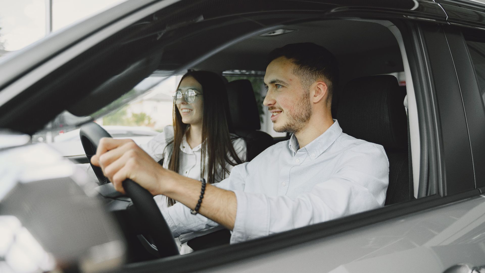 A young couple smiling while driving together in a modern car interior.