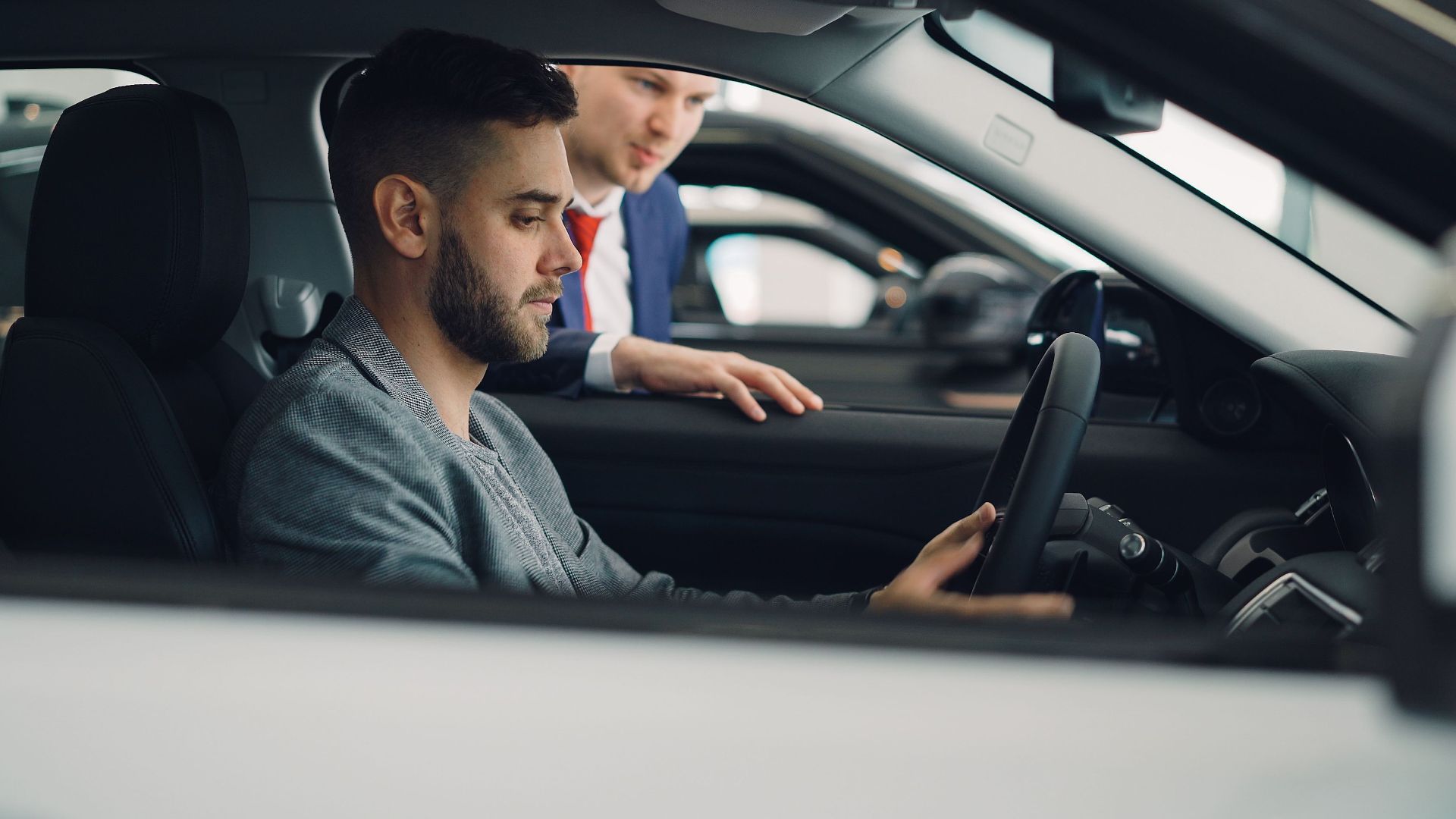 Man examining car interior with salesman at a dealership, highlighting car features.