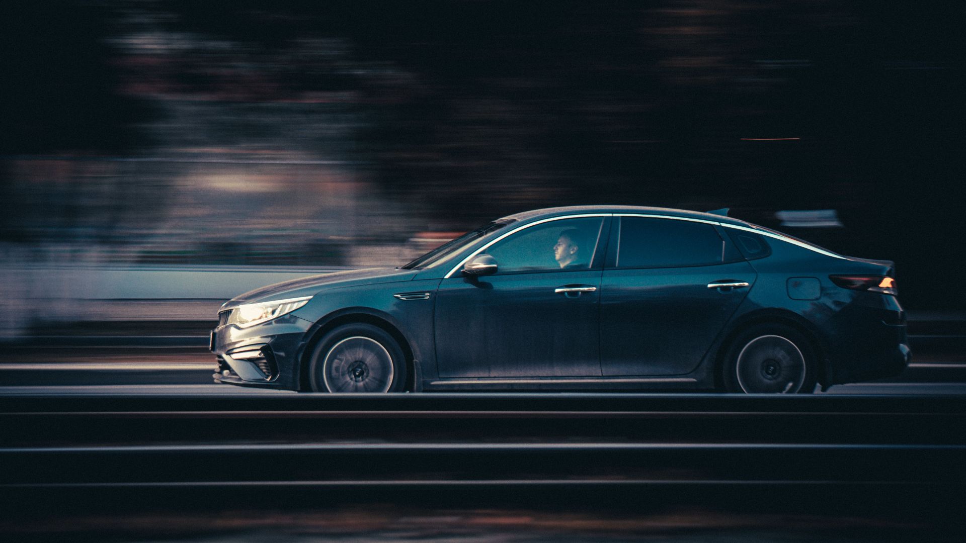 A black car speeds down the road at night, showcasing motion and dynamism.