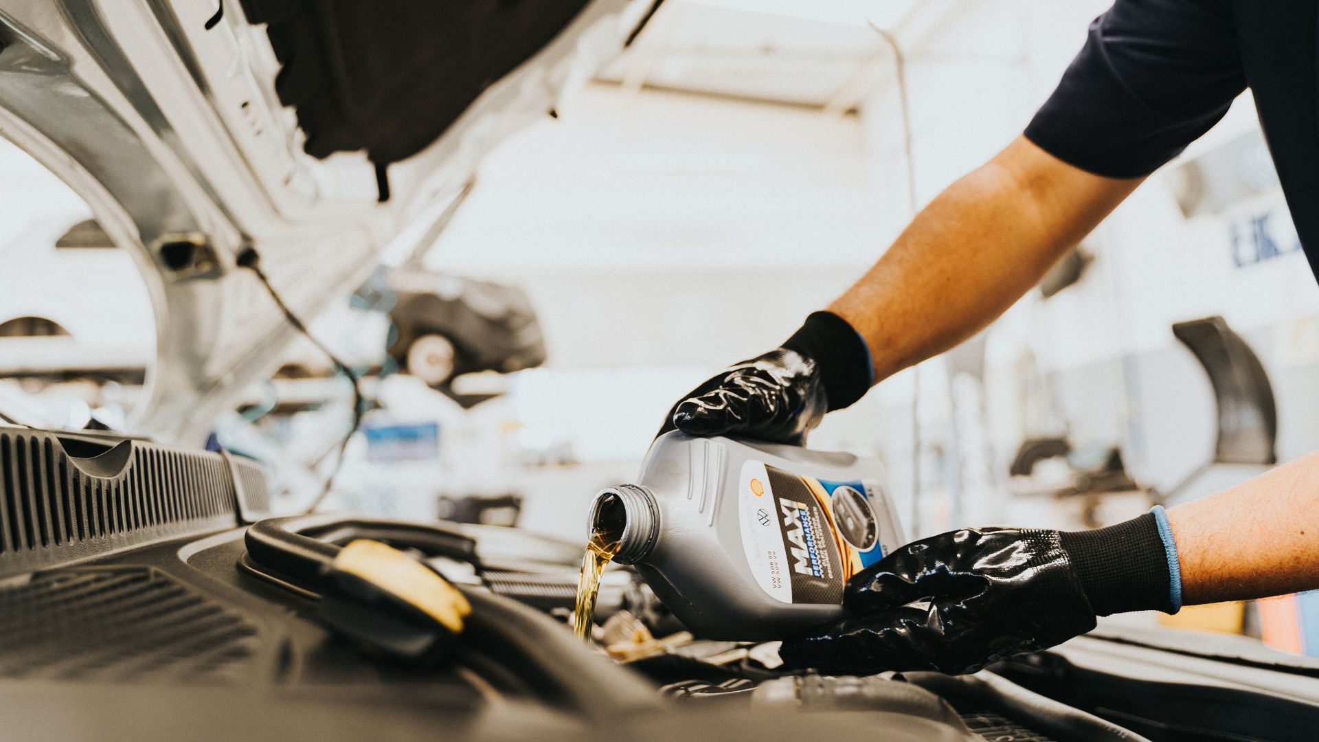 Close-up of a mechanic pouring engine oil in a car inside a garage. Hands wearing gloves.