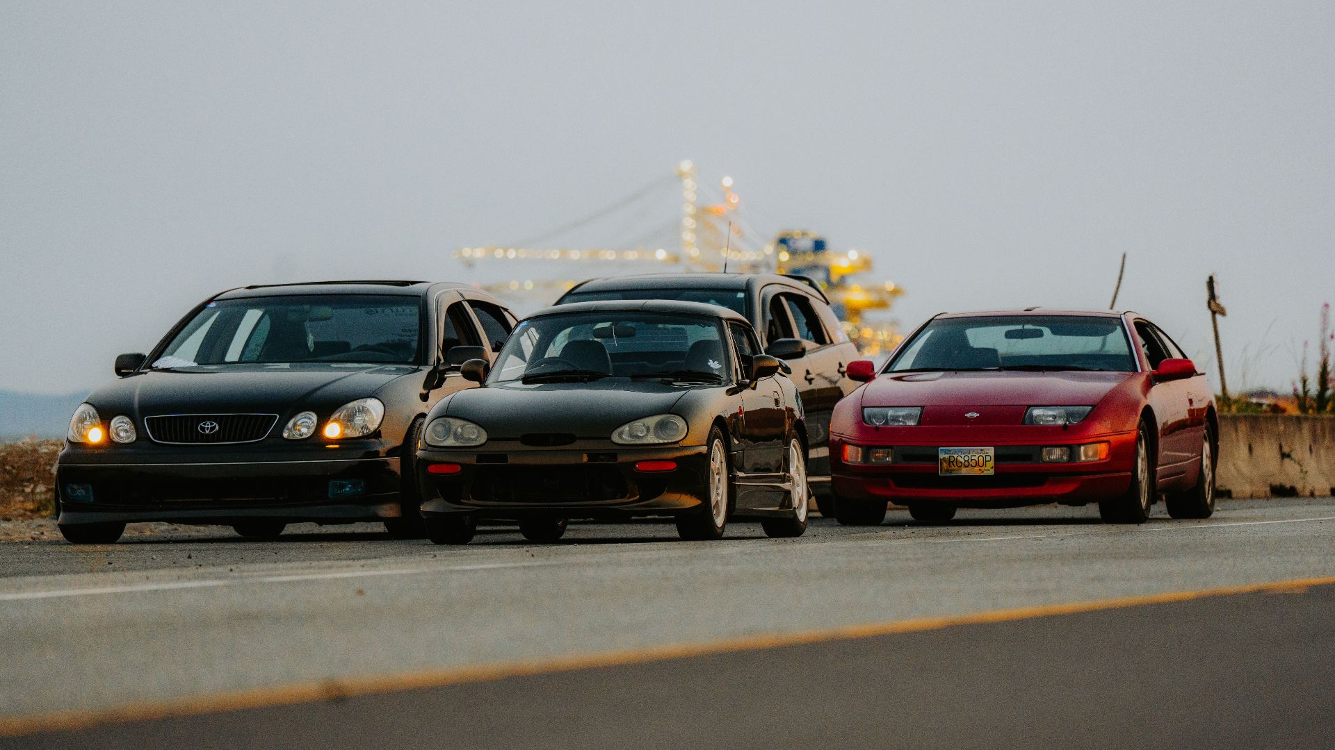 Four classic sports cars line up on a scenic road, ready for adventure.