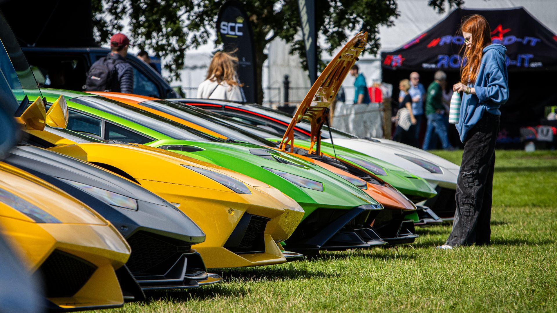 A lineup of colorful Lamborghinis displayed outdoors with onlookers.