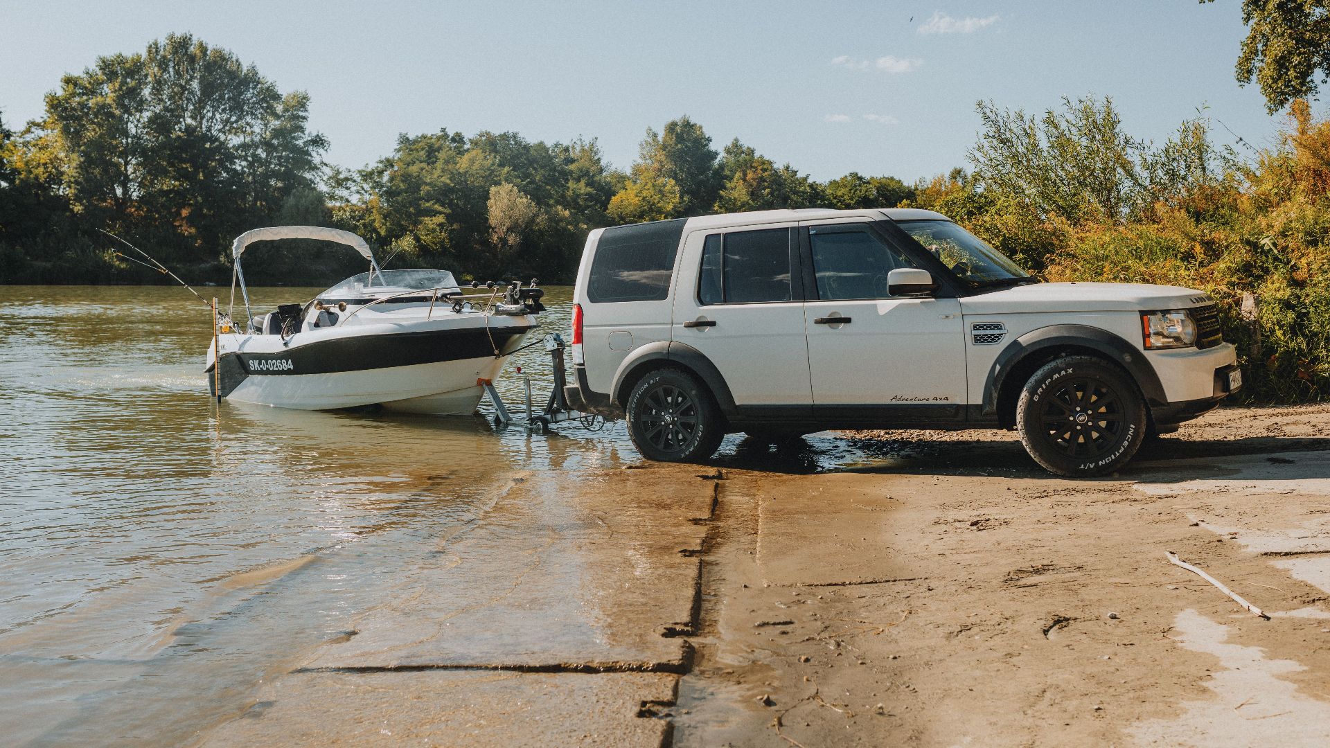 An SUV launching a speedboat into a river on a sunny day, showcasing outdoor adventure.