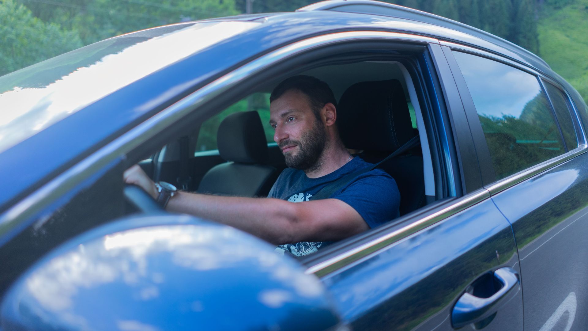 Bearded man enjoying a drive through lush green countryside on a sunny day.