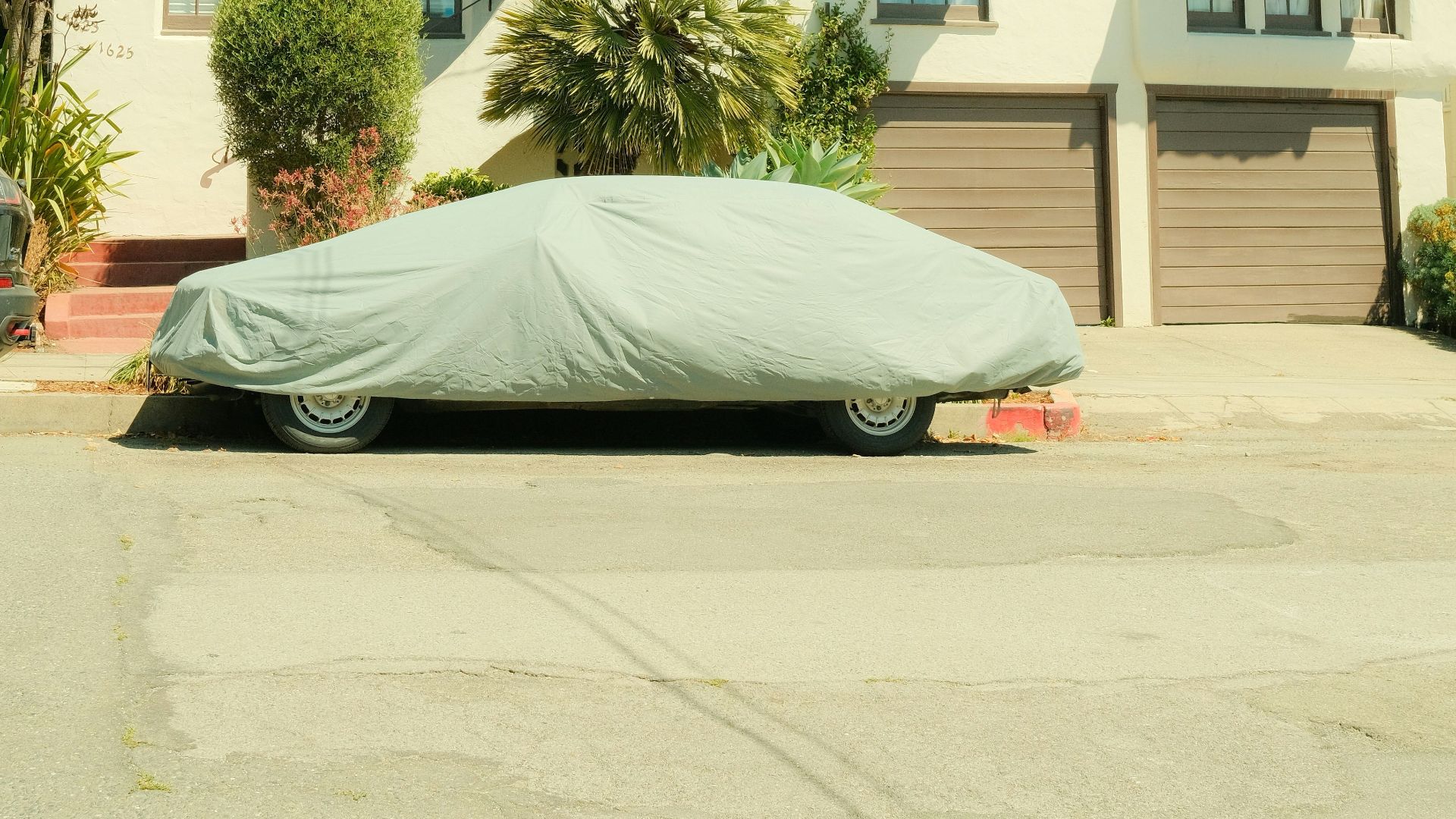 Vintage Mediterranean house with car covered in the driveway under a bright sky.