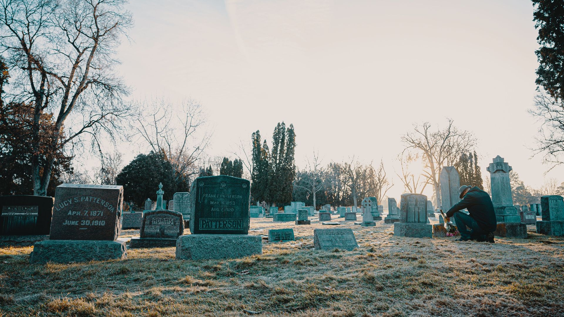 A serene cemetery at sunrise with a person reflecting by a gravestone