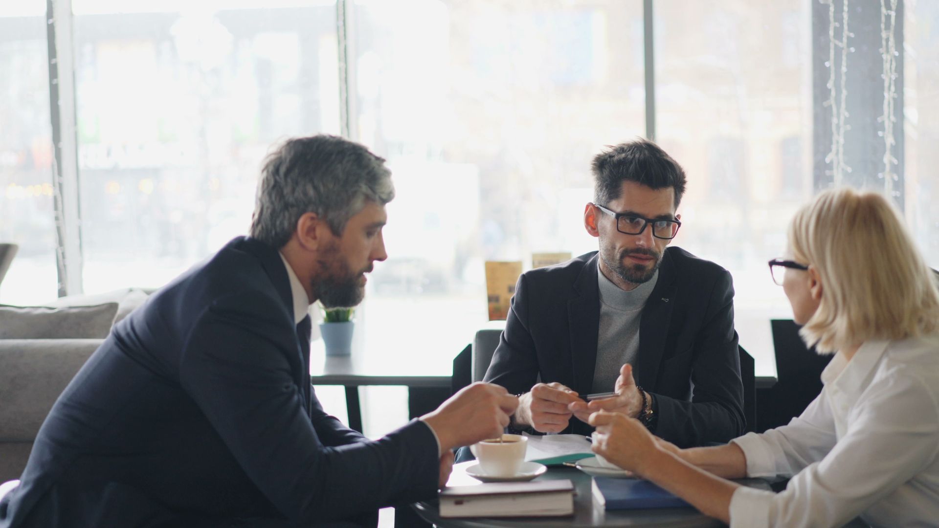 Three professionals engaging in a business discussion over coffee in a modern café setting.