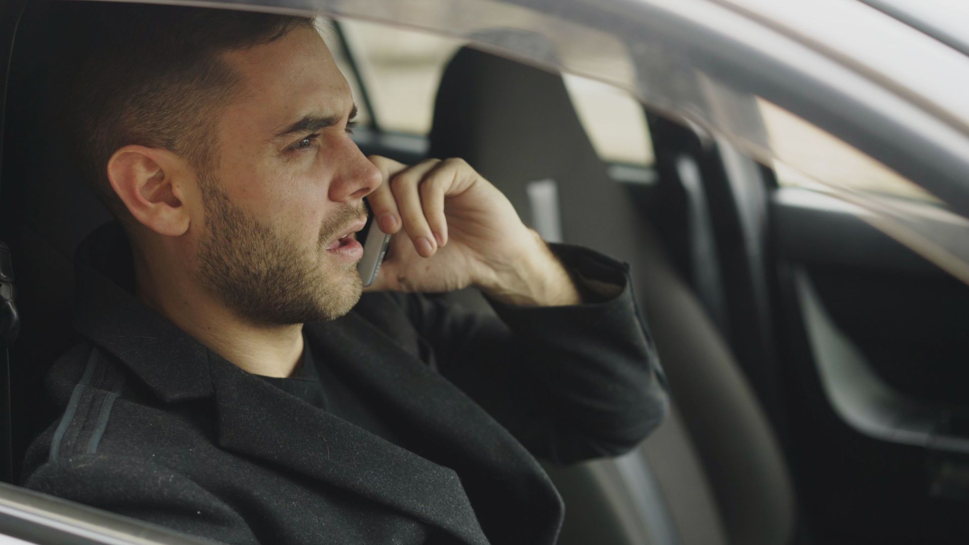 Man in car talking on smartphone, appearing thoughtful.