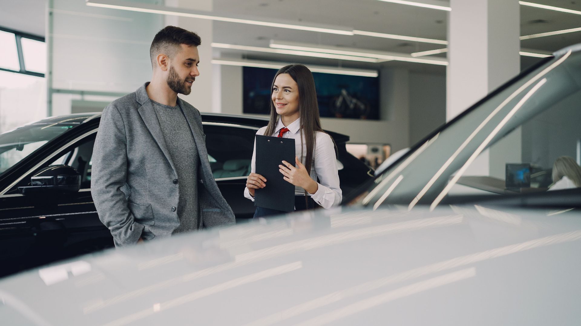 Man consults with salesperson in modern car dealership showroom.