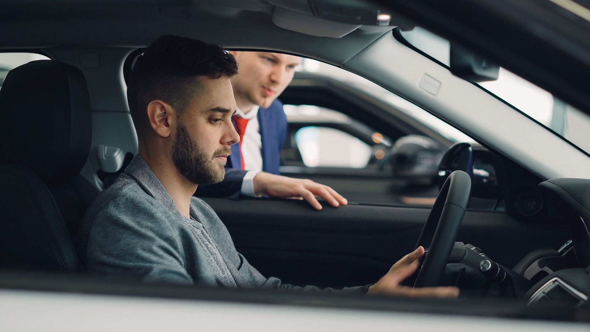 Man examining car interior with salesman at a dealership, highlighting car features.