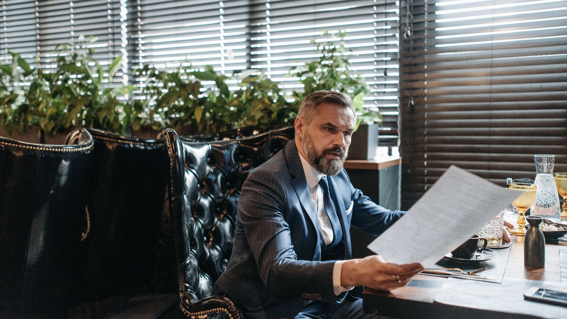 Elderly businessman in a suit analyzing paperwork in a modern office with plants.