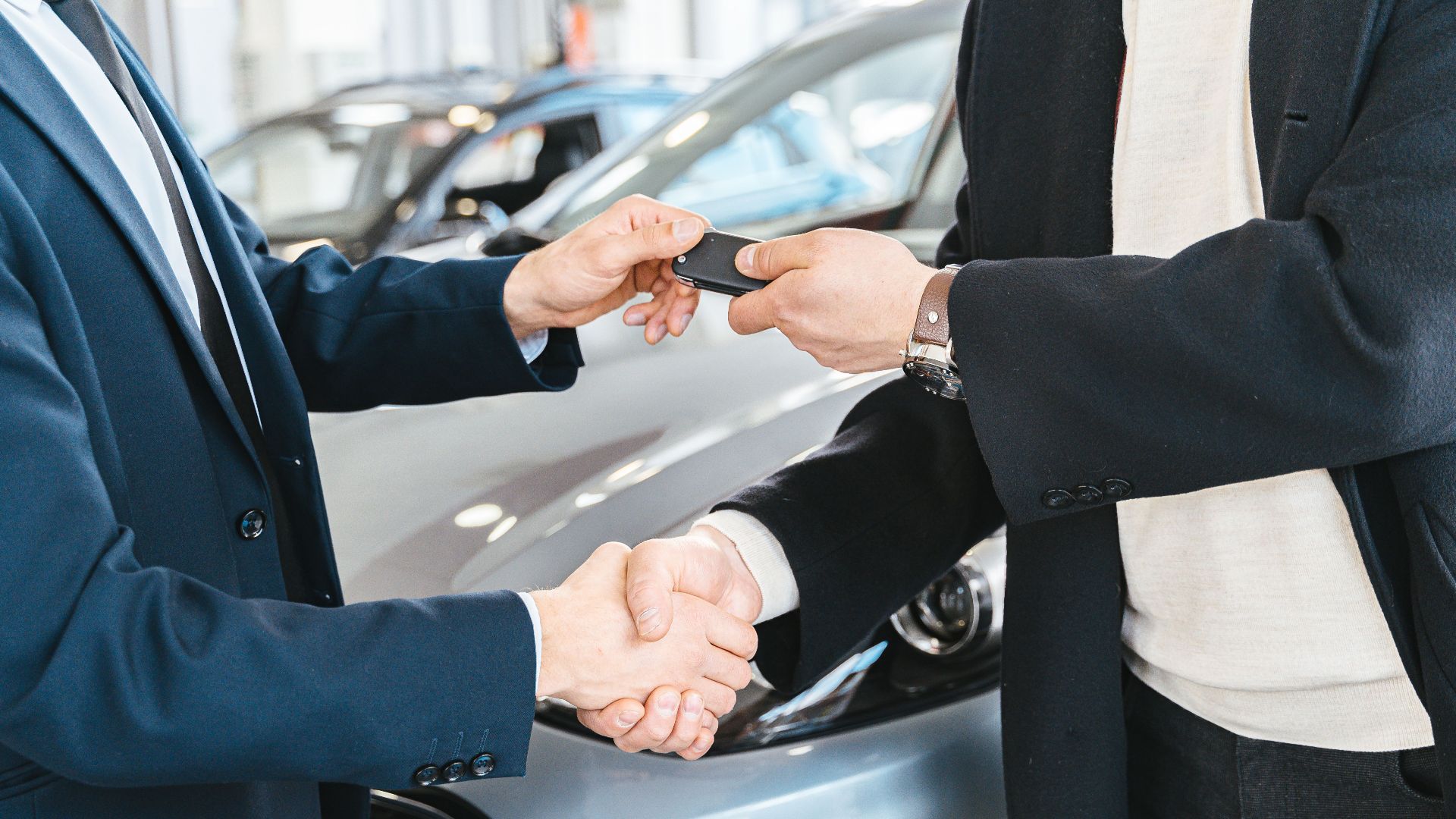 Two businessmen shaking hands and exchanging car keys in a dealership. Symbolizes a successful deal.