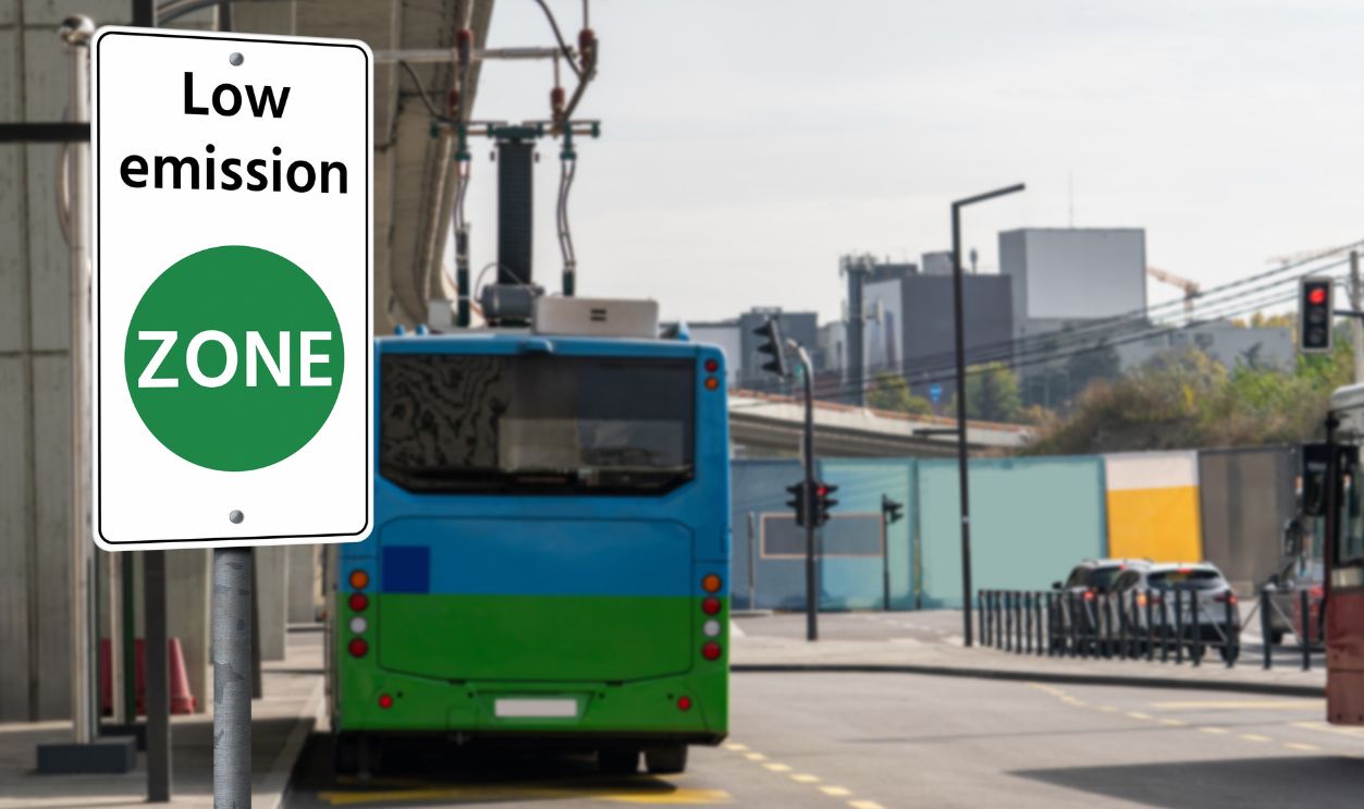 Road sign "Low emission ZONE" on a background of green electric buses. Clean mobility concept .