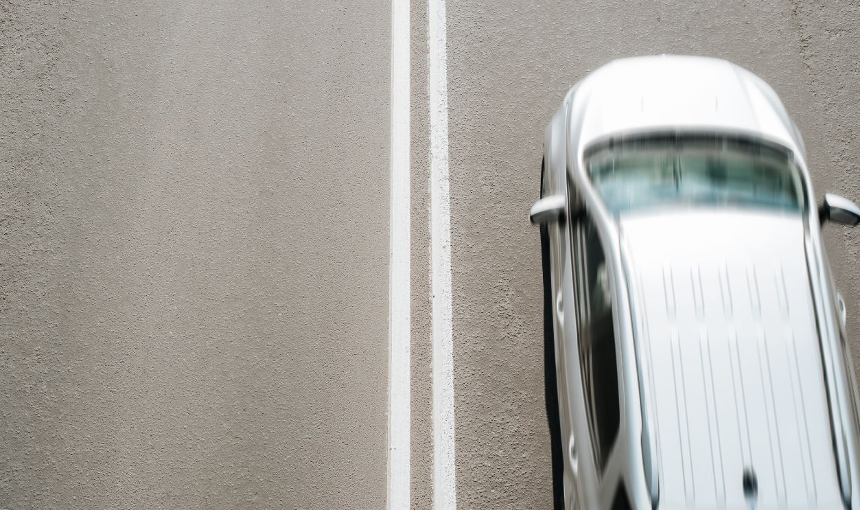 Silvery car driving at fast speed on road, top view. Blurred fast motion, selective focus on dividing double solid marking line on asphalt, copy space.