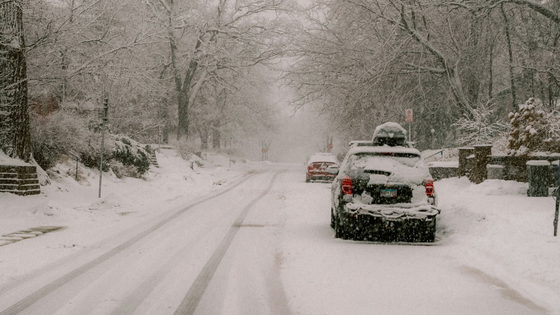 Cars driving on a snowy road during a snowstorm.