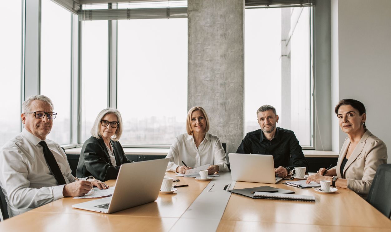 A team of mature business professionals in a meeting around a conference table with laptops 