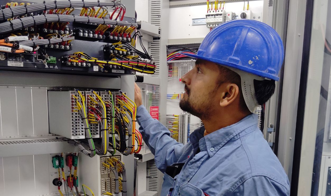 Electrician in blue helmet checking control panel wiring for safety 