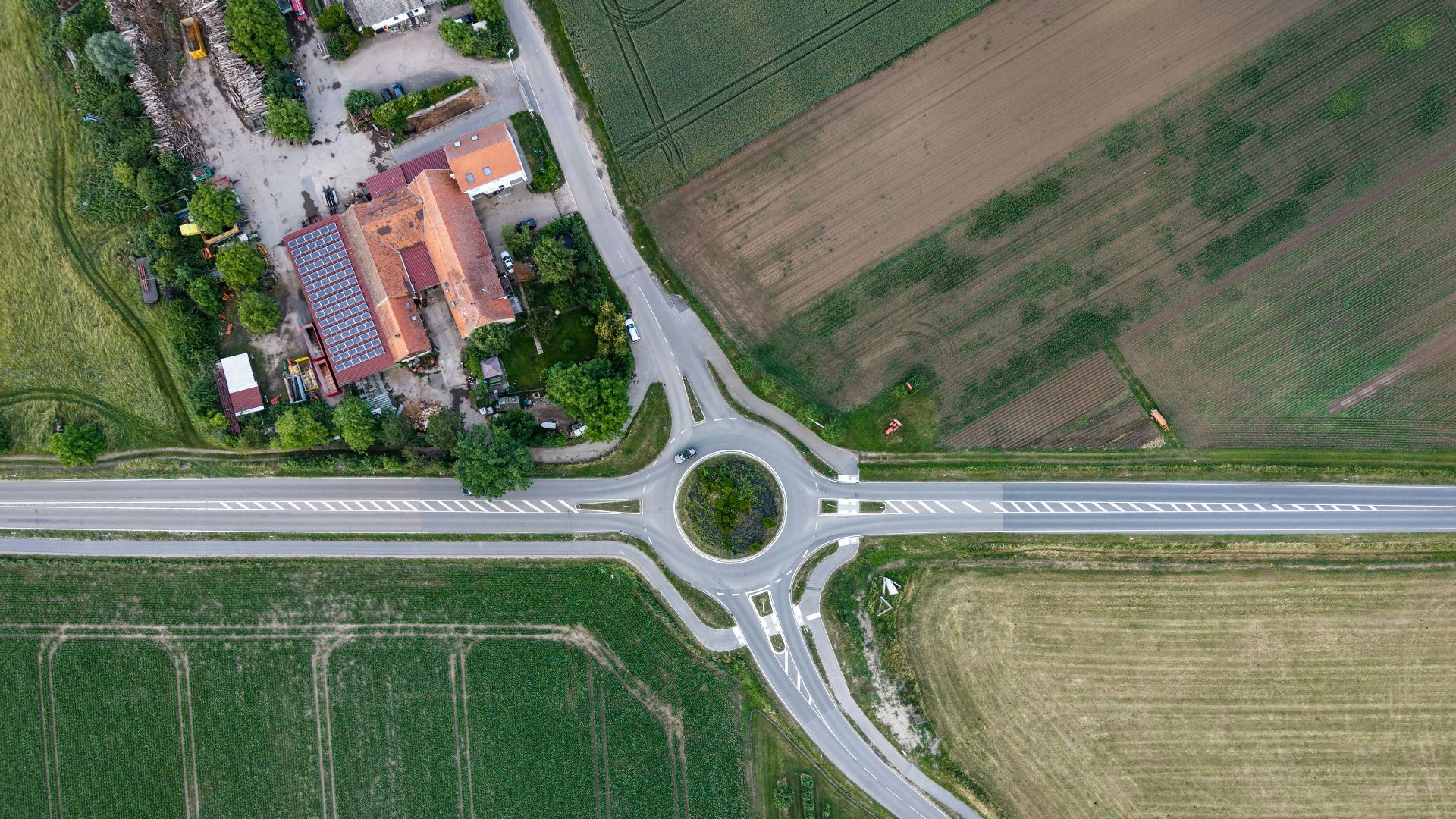 Roundabout connecting roads between green fields and buildings.