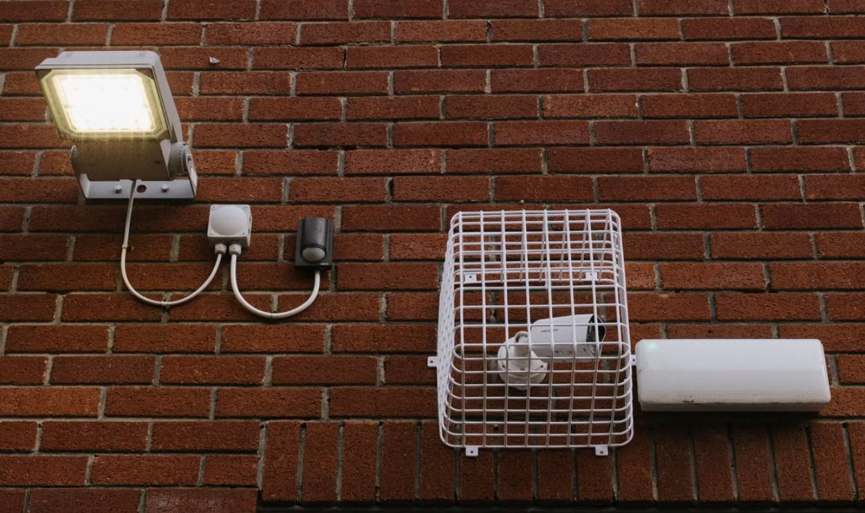 Close-up view of a brick wall featuring a LED light and a caged security camera