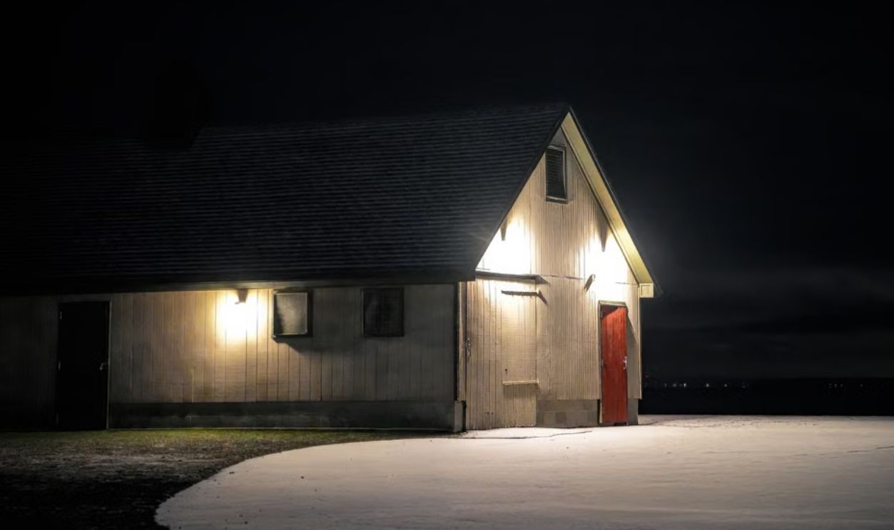 A warmly lit cabin stands alone on a snowy night, offering a peaceful winter scene