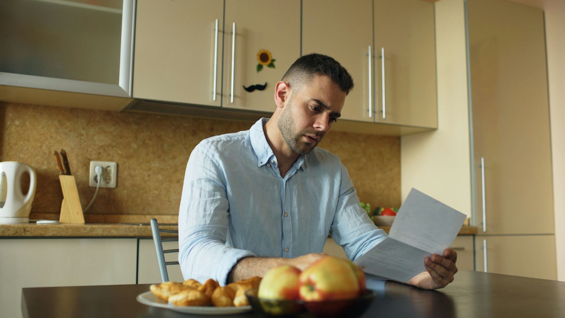 Man reading document at kitchen table with fruit and fruit