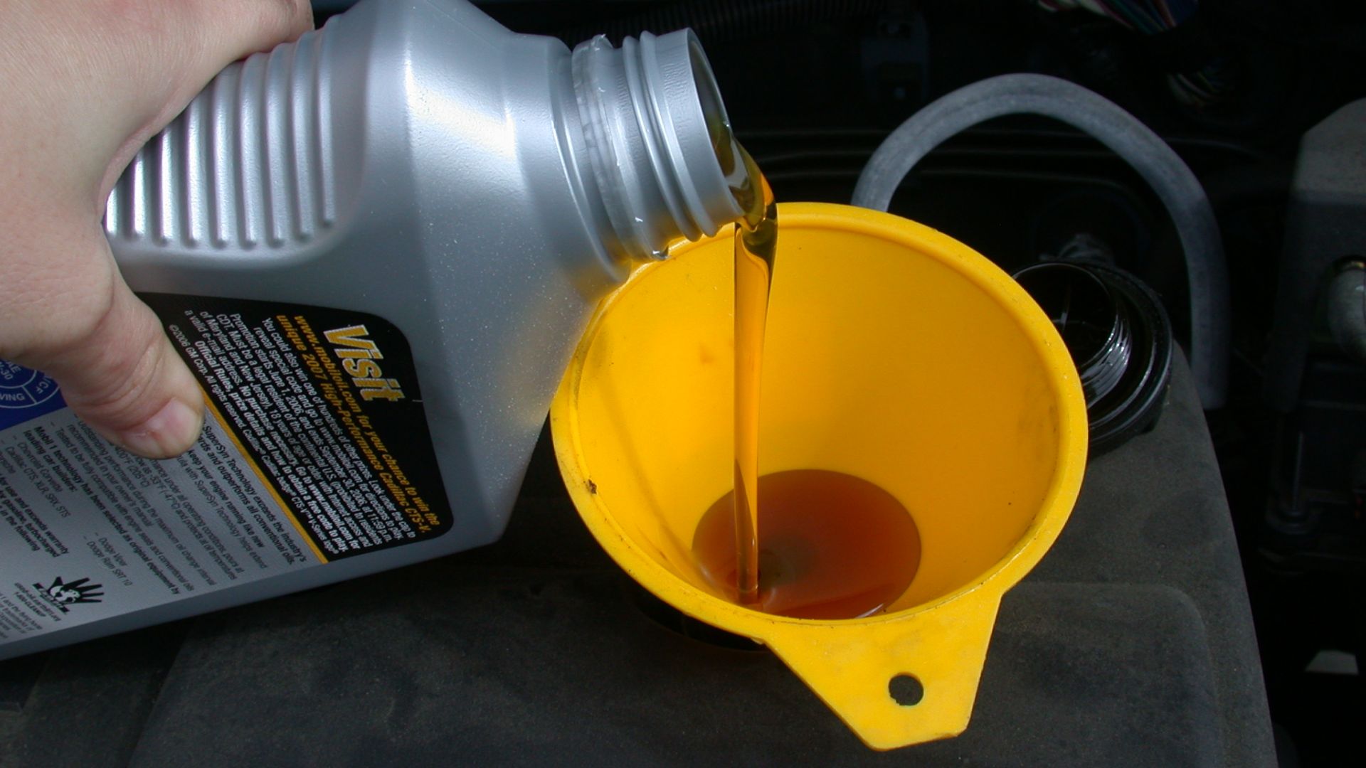 Using a funnel to refill the motor oil in an automobile as part of an oil change.