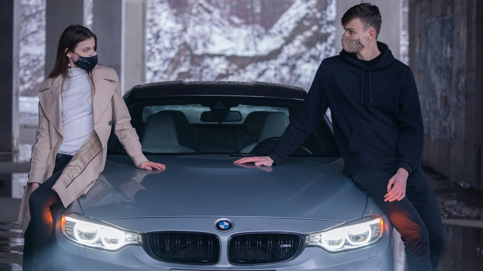 man in black jacket and blue denim jeans sitting on black bmw car