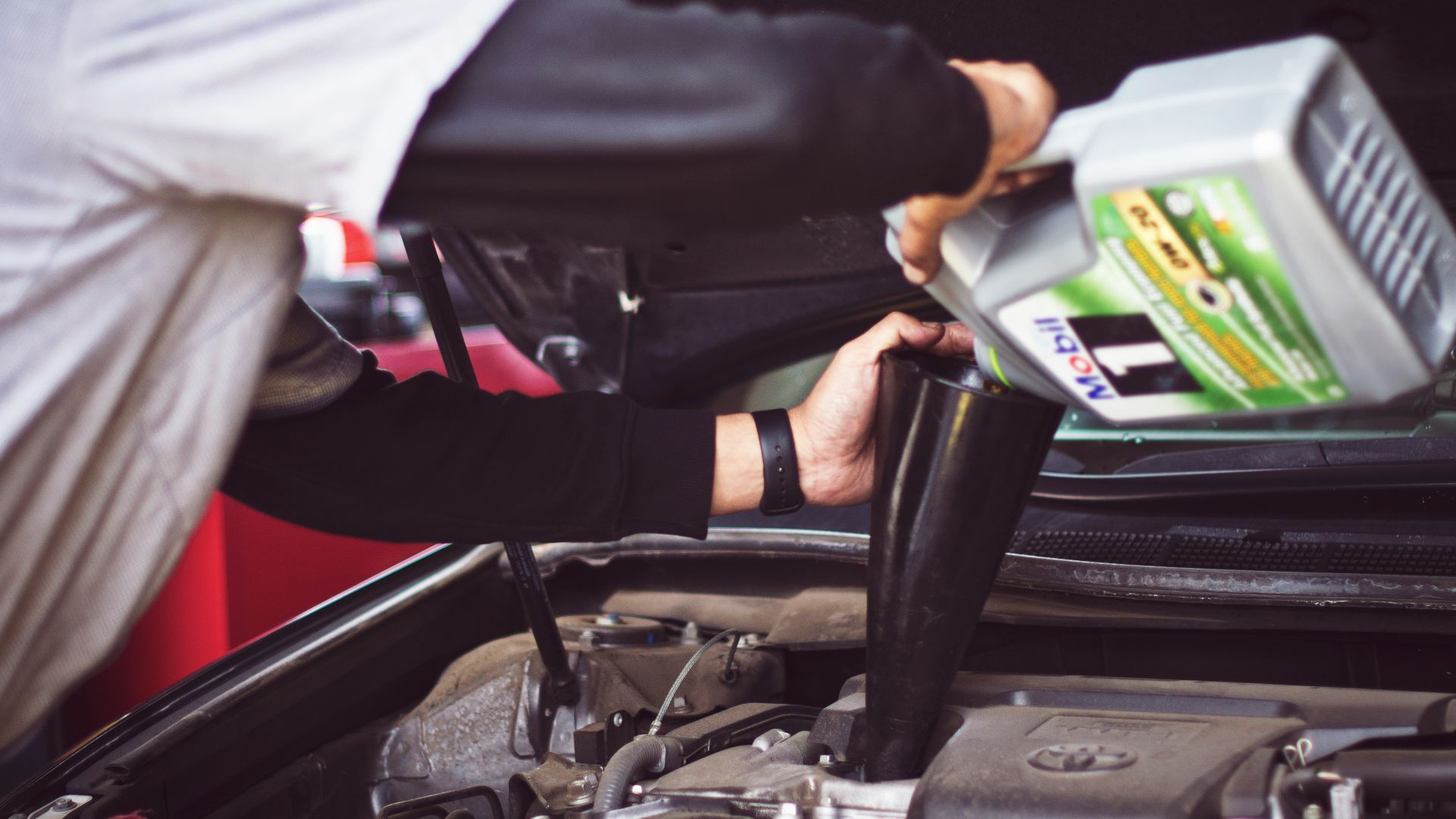 man refilling motor oil on car engine bay