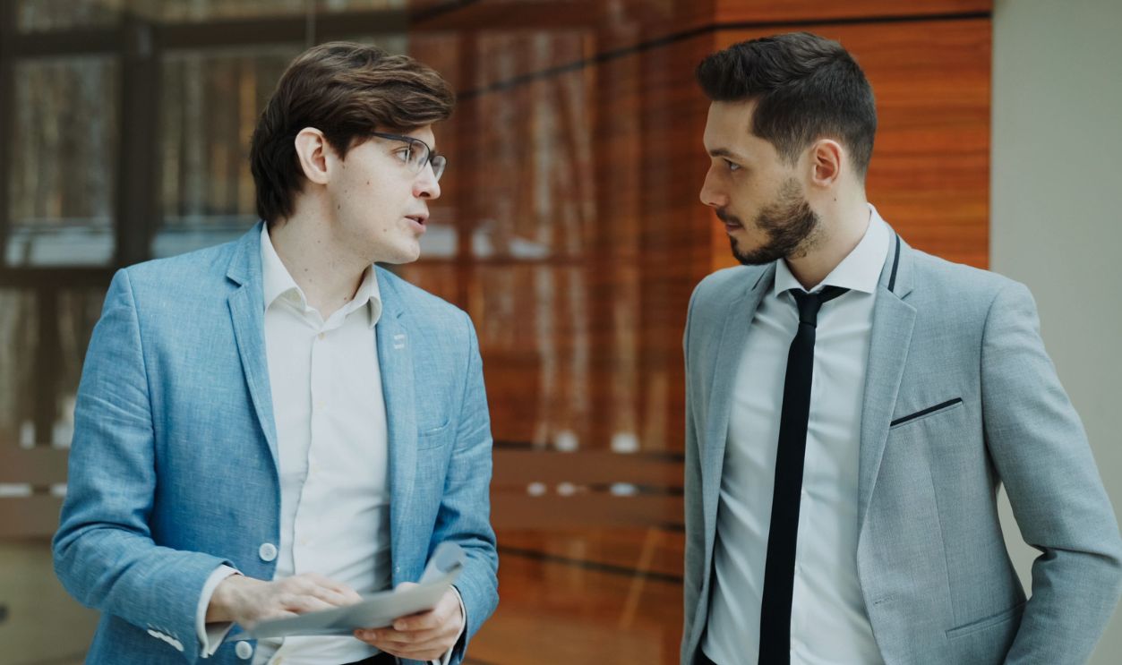 Two businessmen in suits having a conversation indoors, modern office