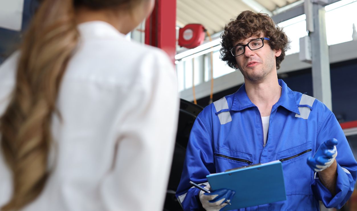 Shutterstock-2207572953, Man technician car mechanical in uniform showing car maintenance service report on clipboard at repair garage station. Auto mechanic give customer discussion on her vehicle repairs problems condition