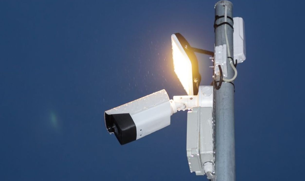 Low angle view of a security camera and light against a dark blue night sky