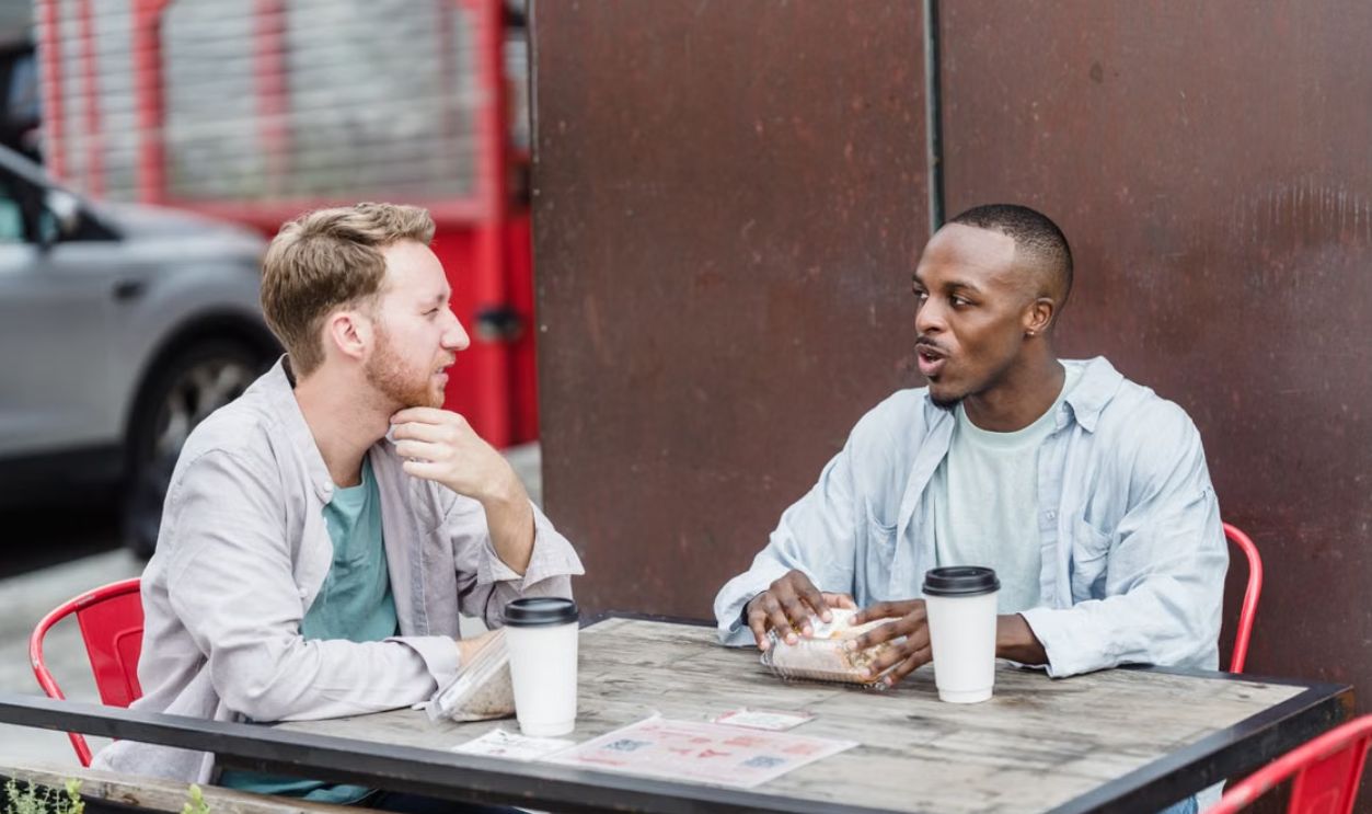 Two men sitting at a table outdoors, drinking coffee and chatting. Perfect for depicting lifestyle and friendship