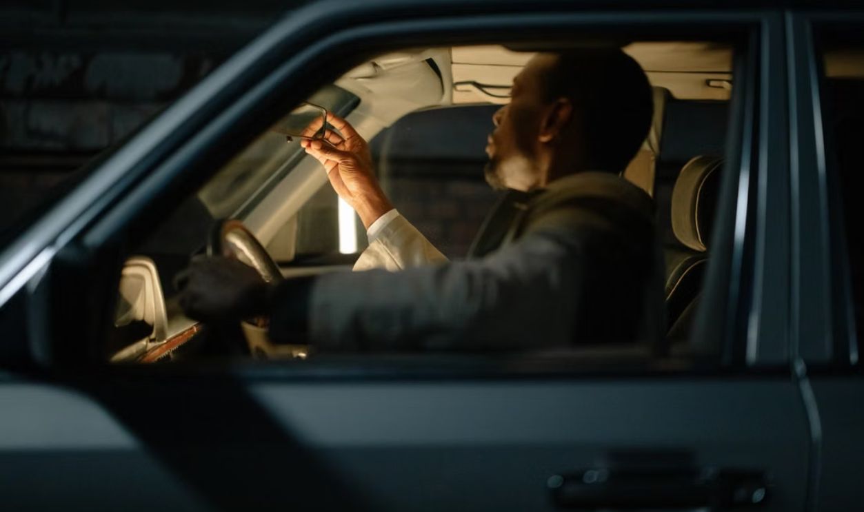 A man sitting inside a car at night adjusting the rearview mirror. Interior illuminated with selective focus.