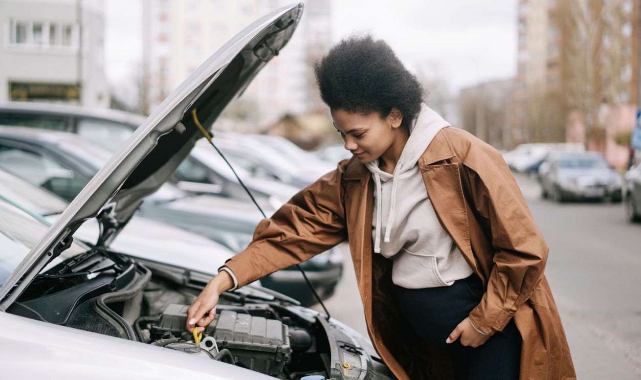 A pregnant woman inspects a car engine outdoors, showcasing independence and car maintenance