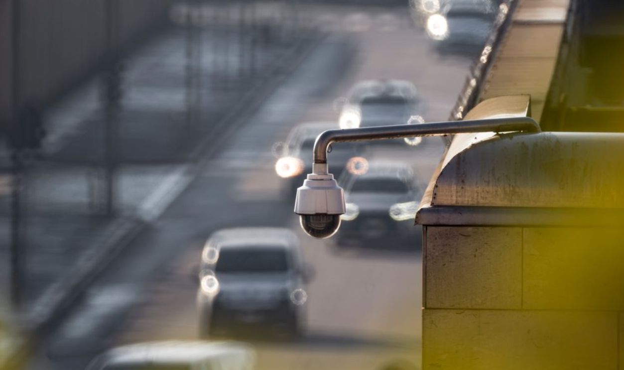 A security camera monitoring activity on a bustling city street with multiple cars in the background