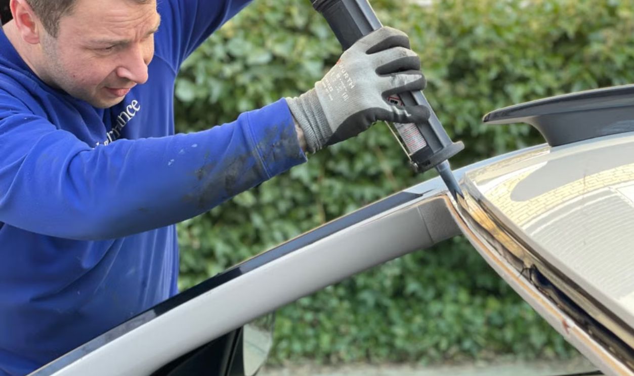Man carefully applies glue to repair car windshield in Copenhagen outdoor setting