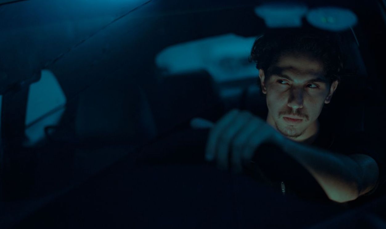 A man focuses intently while driving a car at night, illuminated by dim blue lighting