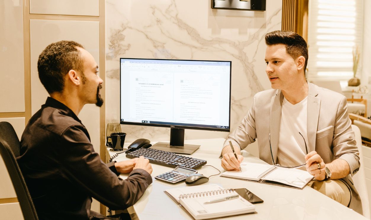 Two businessmen discussing work at a sleek and modern office desk, using computer and notes