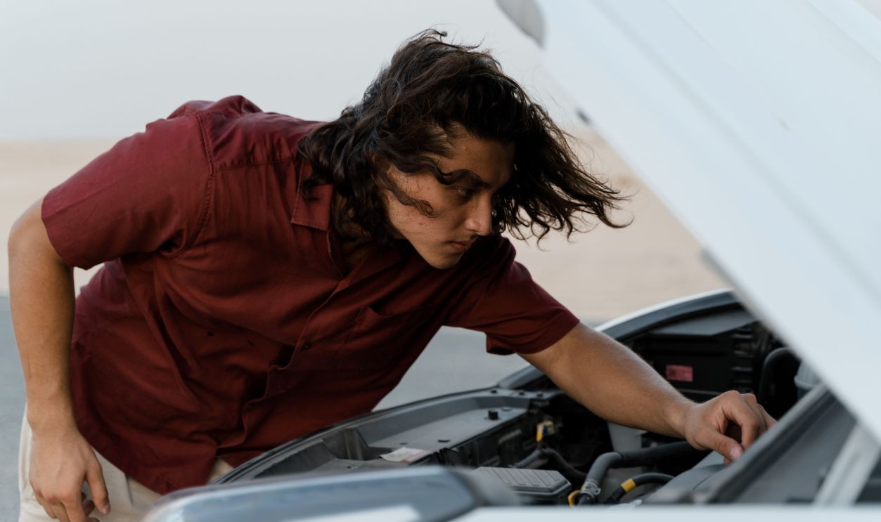 Person checking under the hood of a car for maintenance outdoors