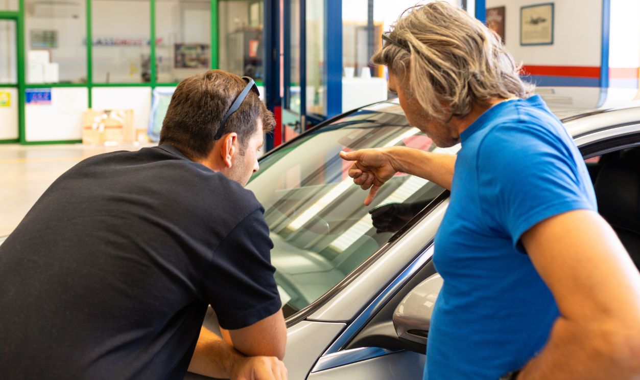 Automobile glazier repairman teaching or discussing with partner windscreen repair of a car in auto service station garage