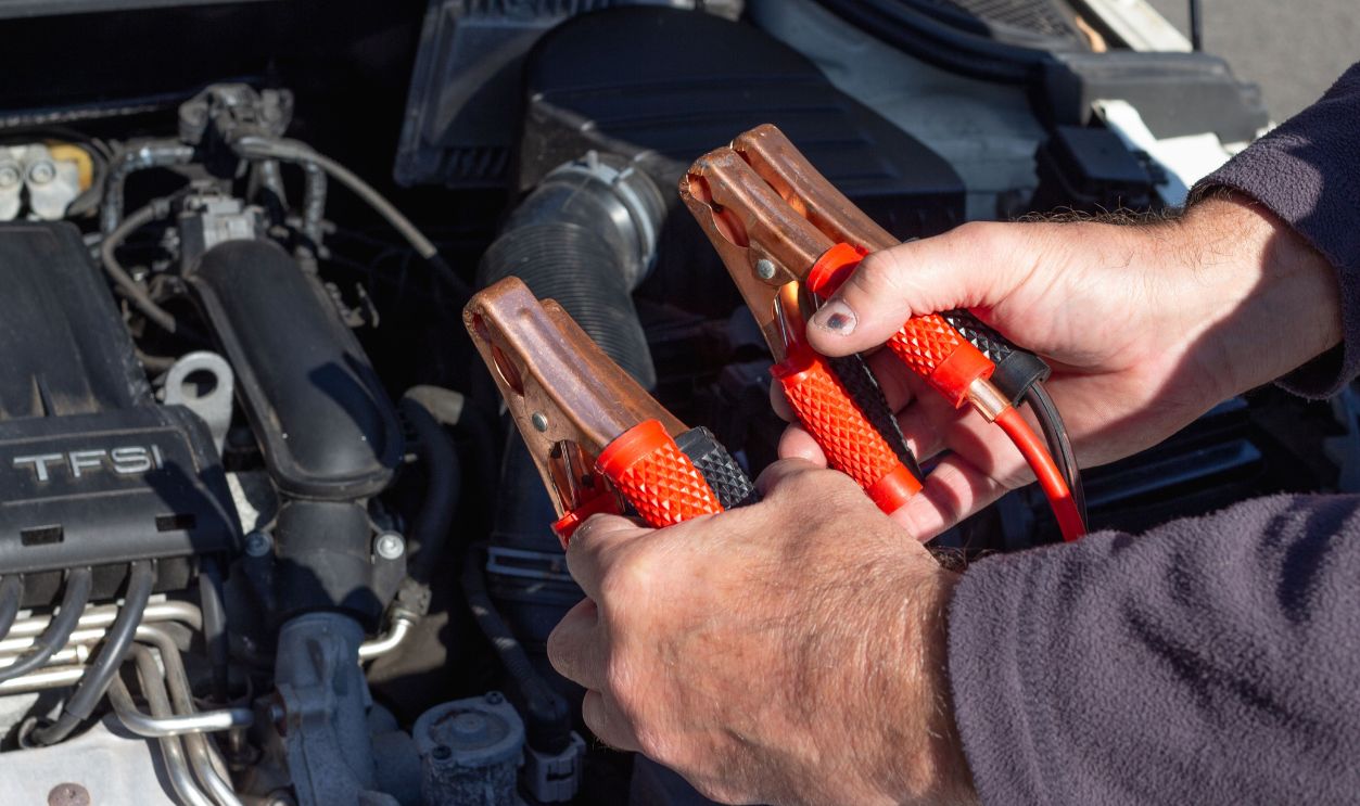 Close-up of hands holding jumper cables near a car engine
