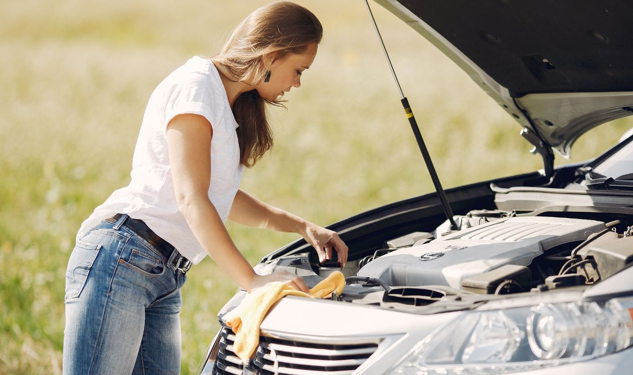 Young woman checking car engine in a sunny countryside setting