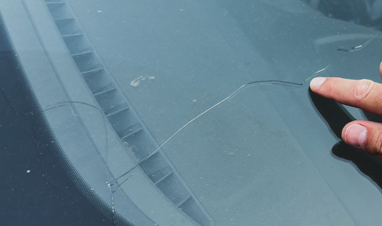 Shutterstock-2640400661, Man s hand pointing at a long crack on a car windshield, highlighting damage on the glass surface under daylight, automotive concept