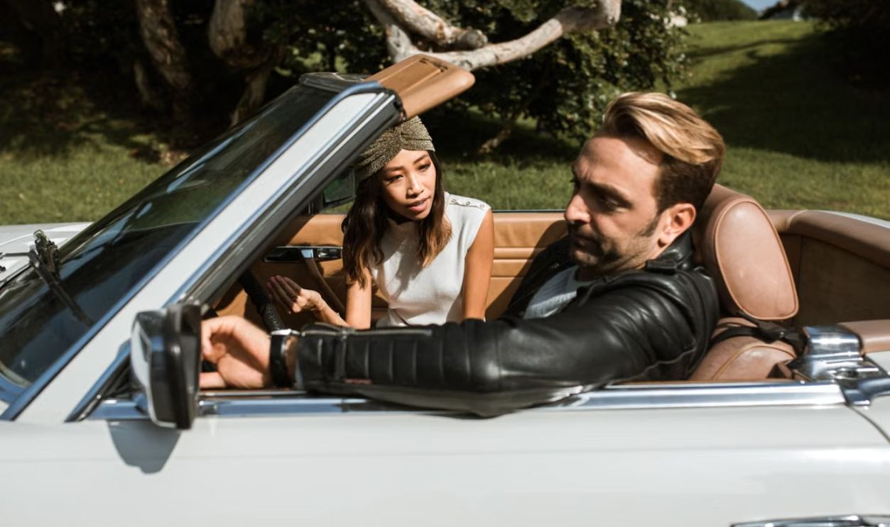A couple engaged in a serious conversation while seated in a convertible on a sunny day.