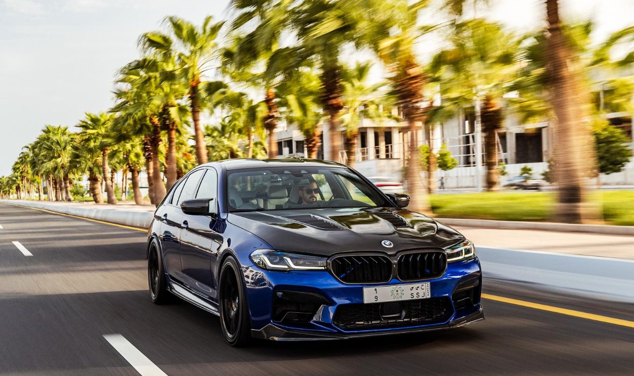 Dynamic shot of a blue car speeding down a palm-lined street in Kuwait City, exuding elegance and performance.