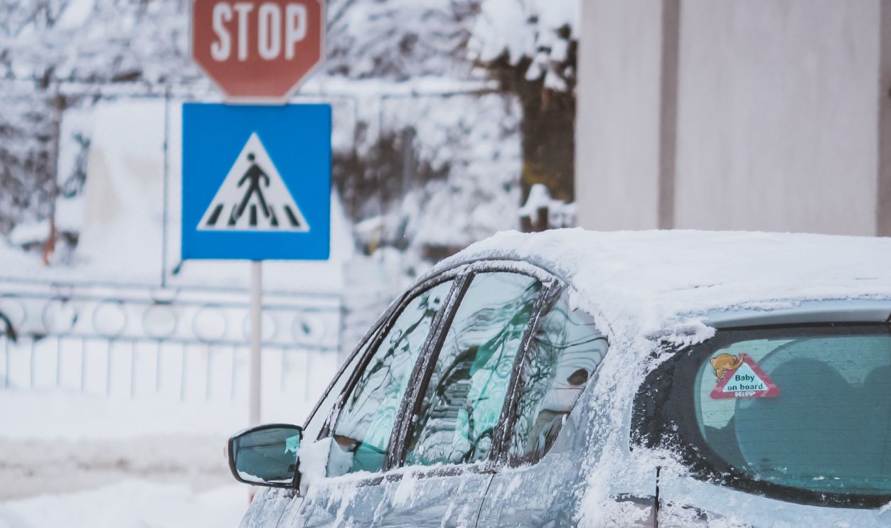 Car moves on snowy road near stop sign in winter, showcasing winter driving conditions.