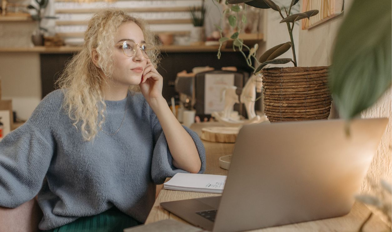 Young woman writing notes on a laptop in a cozy cafe setting. Ideal for small business
