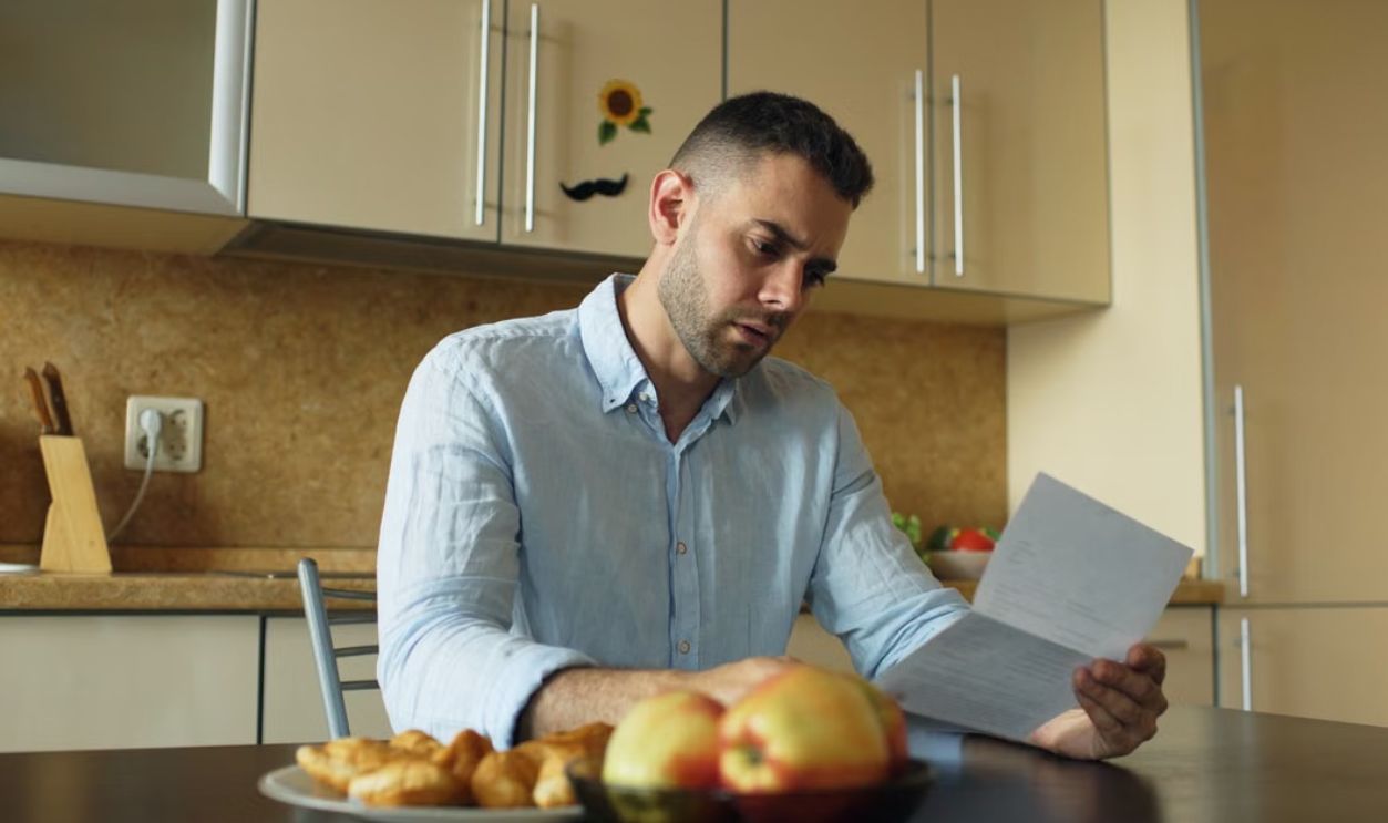 Man in a kitchen reading a document, apples on table