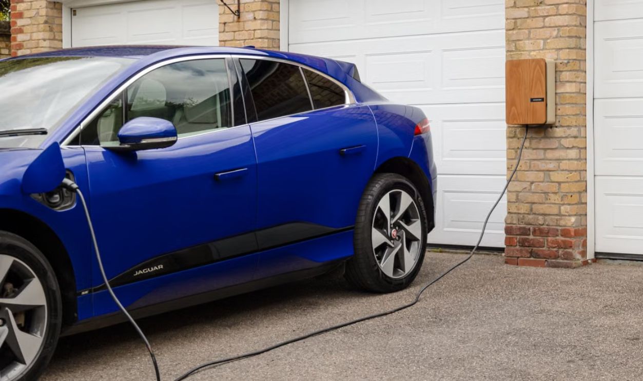 Blue electric vehicle charging at home using wall-mounted unit. Sustainable transportation solution